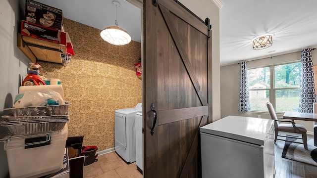 clothes washing area featuring light tile patterned floors, a barn door, separate washer and dryer, and ornamental molding