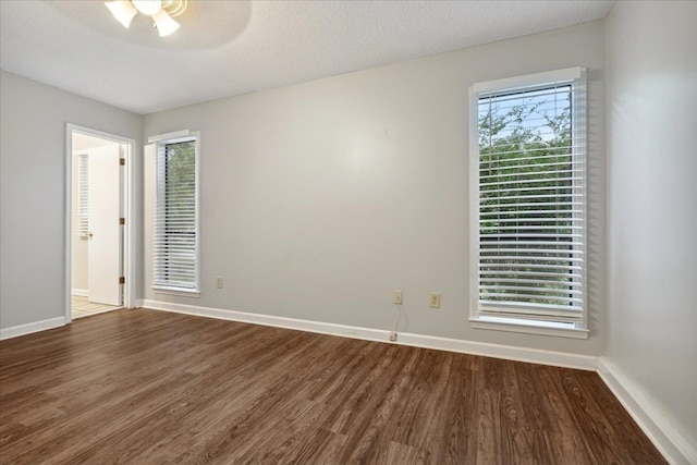 empty room with a textured ceiling, plenty of natural light, and dark hardwood / wood-style flooring