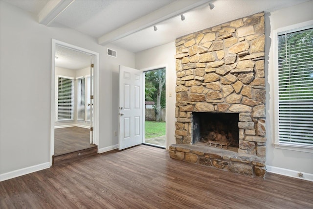 unfurnished living room with a stone fireplace, a textured ceiling, beamed ceiling, and dark hardwood / wood-style flooring