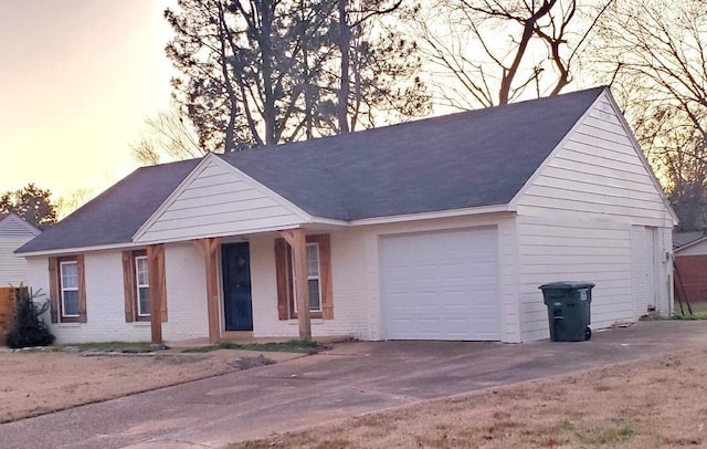 ranch-style house featuring brick siding, an attached garage, a shingled roof, and driveway