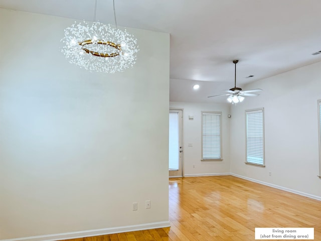 empty room with light wood-type flooring and ceiling fan with notable chandelier