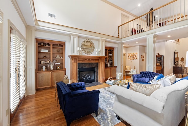 living room featuring a high end fireplace, ornate columns, crown molding, a high ceiling, and hardwood / wood-style flooring