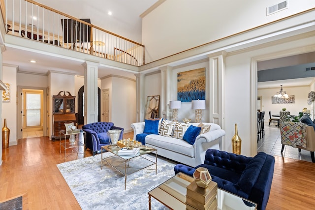 living room with ornamental molding, hardwood / wood-style flooring, decorative columns, an inviting chandelier, and a towering ceiling