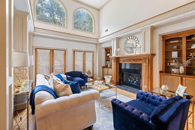 living room featuring light hardwood / wood-style flooring, crown molding, a high ceiling, and a high end fireplace