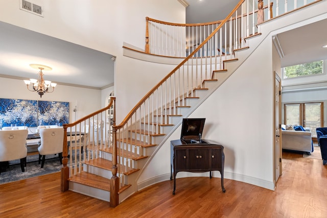 staircase with a notable chandelier, a high ceiling, ornamental molding, and hardwood / wood-style flooring