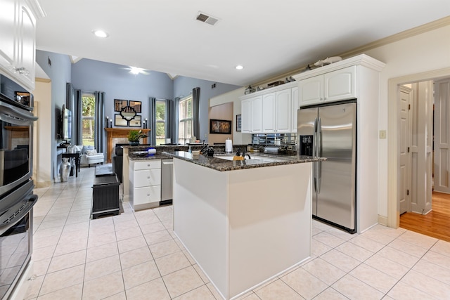 kitchen featuring dark stone countertops, white cabinets, stainless steel fridge, and light tile patterned floors