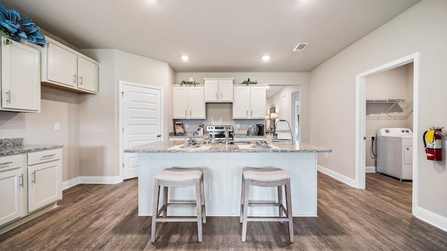 kitchen with light stone countertops, a kitchen island with sink, and dark wood-type flooring