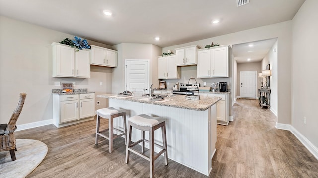 kitchen featuring light stone counters, a kitchen island with sink, light hardwood / wood-style floors, and white cabinetry