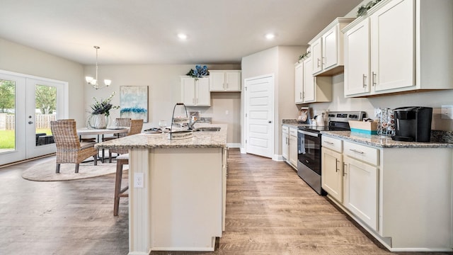 kitchen with hanging light fixtures, light stone countertops, light hardwood / wood-style flooring, a kitchen island with sink, and stainless steel range with electric cooktop