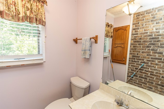 bathroom featuring brick wall, ornamental molding, vanity, and toilet