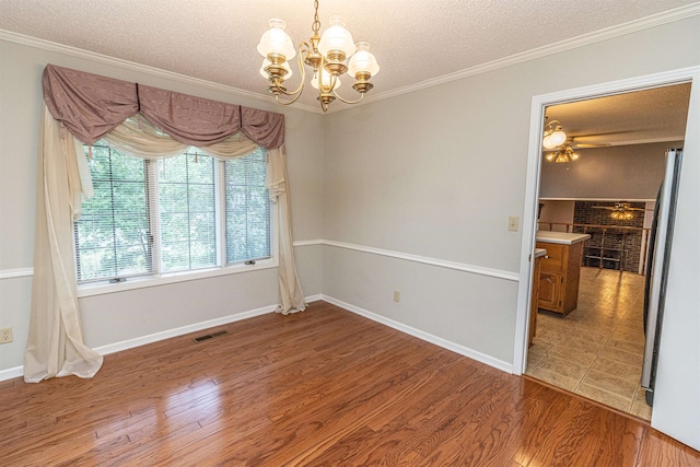 spare room featuring a textured ceiling, ornamental molding, hardwood / wood-style floors, and an inviting chandelier