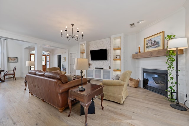 living room with light hardwood / wood-style floors, ornamental molding, a large fireplace, and a notable chandelier