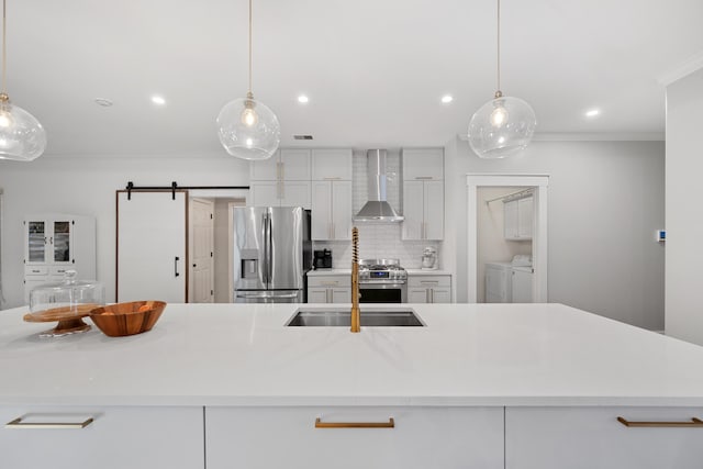 kitchen featuring decorative light fixtures, wall chimney exhaust hood, washer and clothes dryer, appliances with stainless steel finishes, and a barn door