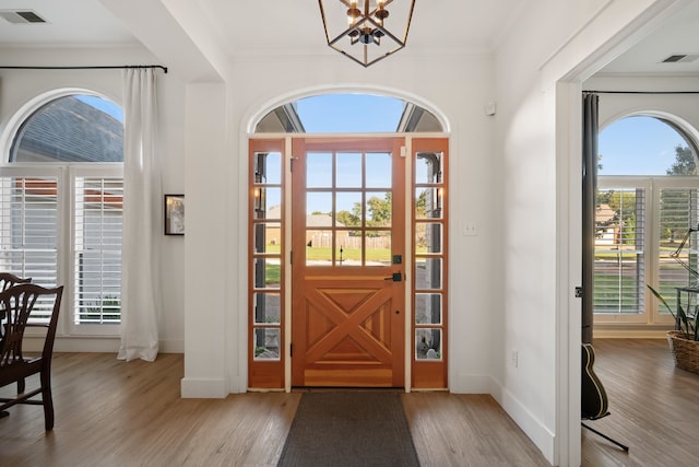 entryway featuring light wood-type flooring, a chandelier, and crown molding