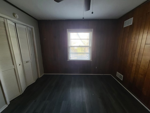 unfurnished bedroom featuring ceiling fan, a closet, wooden walls, and dark wood-type flooring