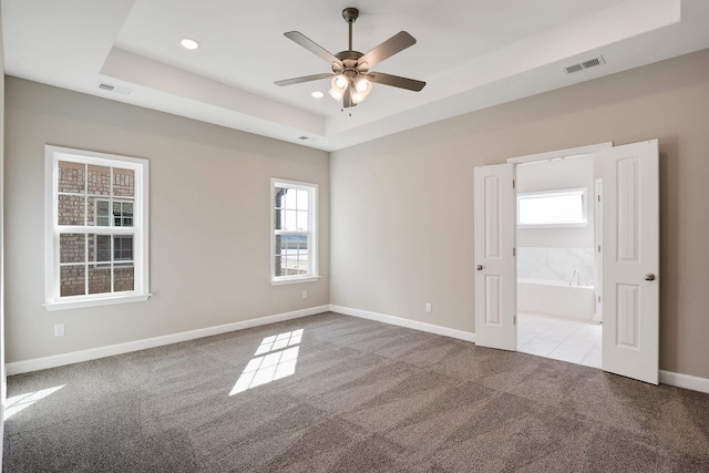 carpeted empty room featuring ceiling fan and a raised ceiling