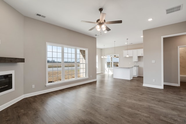 unfurnished living room with ceiling fan with notable chandelier and dark hardwood / wood-style flooring