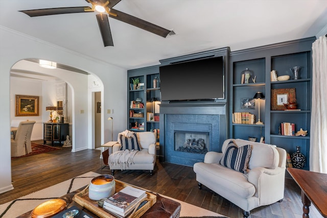 living room featuring built in shelves, crown molding, dark wood-type flooring, and ceiling fan