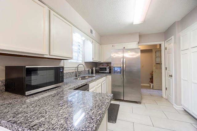 kitchen featuring a textured ceiling, sink, white cabinetry, stainless steel appliances, and dark stone countertops