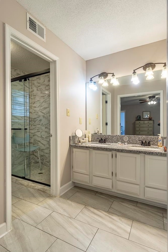 bathroom featuring ceiling fan, vanity, a shower with shower door, and a textured ceiling