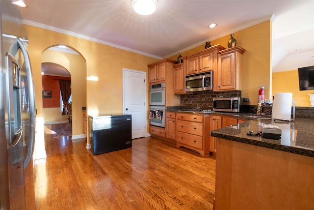 kitchen with dark stone counters, light hardwood / wood-style flooring, decorative backsplash, appliances with stainless steel finishes, and ornamental molding