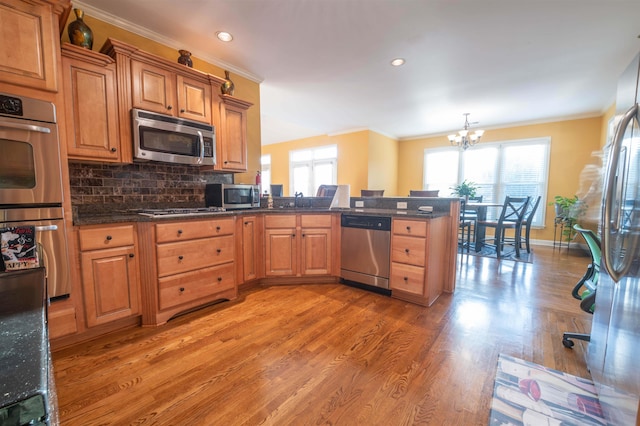 kitchen featuring hanging light fixtures, tasteful backsplash, stainless steel appliances, an inviting chandelier, and hardwood / wood-style flooring