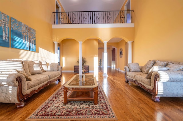 living room featuring hardwood / wood-style flooring, a towering ceiling, and ornate columns