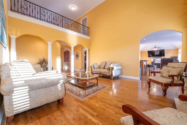 living room with wood-type flooring, ceiling fan, a high ceiling, and ornate columns