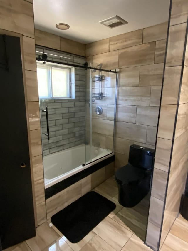 bathroom with tile walls, tile patterned flooring, toilet, and combined bath / shower with glass door