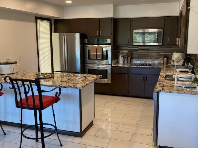 kitchen with appliances with stainless steel finishes, dark brown cabinetry, sink, and light stone counters