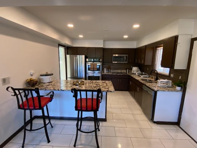 kitchen with appliances with stainless steel finishes, a breakfast bar area, sink, and light stone counters