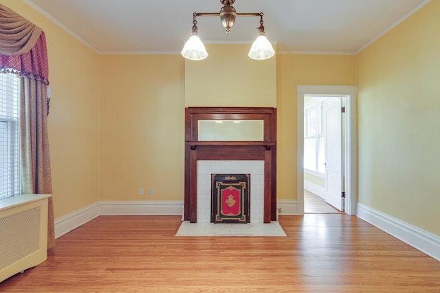 unfurnished living room with crown molding, a fireplace, radiator, and light hardwood / wood-style flooring