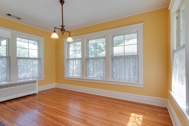 unfurnished dining area featuring crown molding, light hardwood / wood-style floors, radiator, and an inviting chandelier