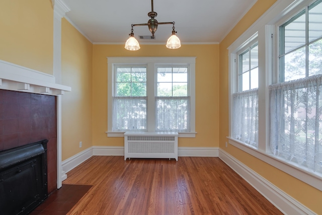 unfurnished living room featuring radiator heating unit, wood-type flooring, a healthy amount of sunlight, and crown molding