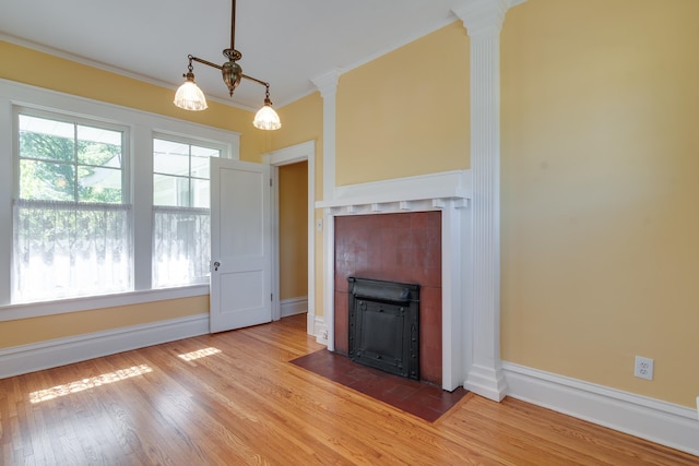 unfurnished living room featuring hardwood / wood-style flooring, decorative columns, ornamental molding, and a tile fireplace