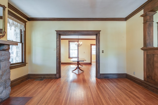 spare room featuring an inviting chandelier, hardwood / wood-style flooring, crown molding, and ornate columns