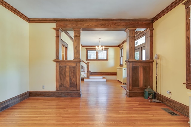 unfurnished room featuring crown molding, light hardwood / wood-style floors, an inviting chandelier, and ornate columns