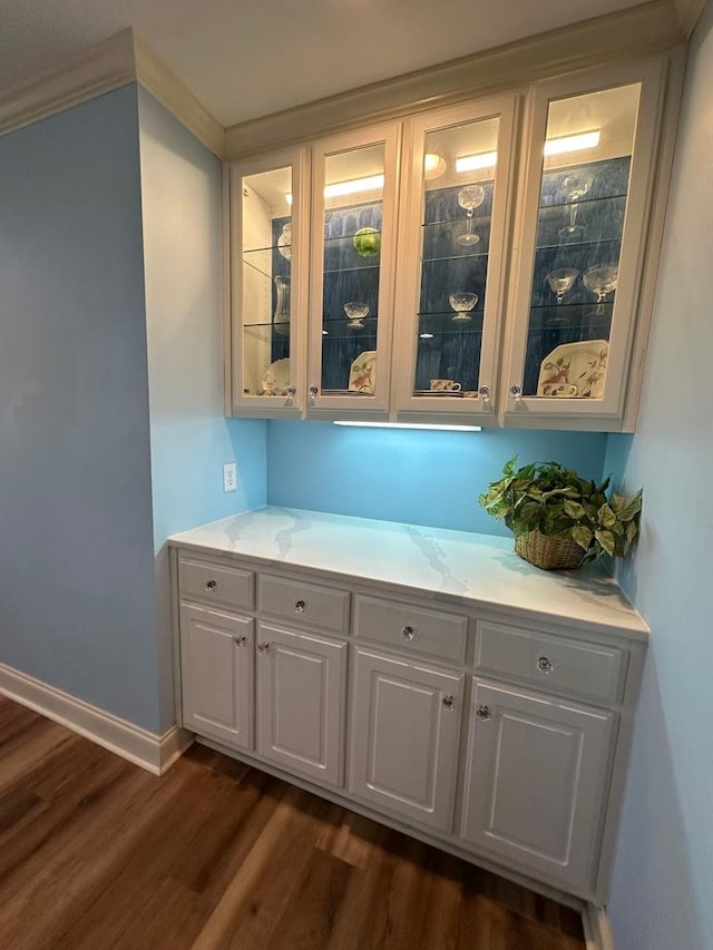 bar featuring crown molding, dark hardwood / wood-style flooring, and white cabinetry