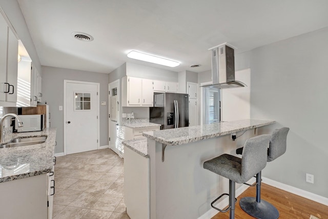 kitchen with light stone counters, white cabinets, stainless steel refrigerator with ice dispenser, and sink