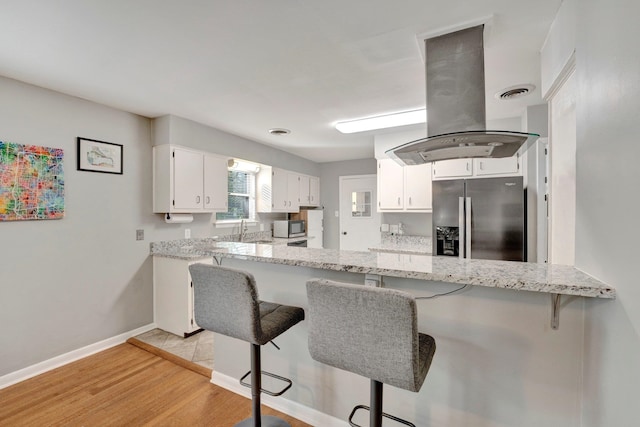 kitchen with light wood-type flooring, white cabinets, island range hood, kitchen peninsula, and stainless steel appliances