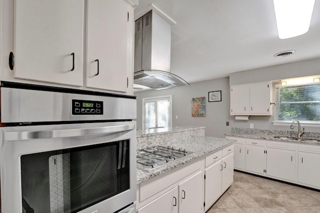 kitchen featuring white cabinets, wall chimney exhaust hood, stainless steel appliances, a healthy amount of sunlight, and sink