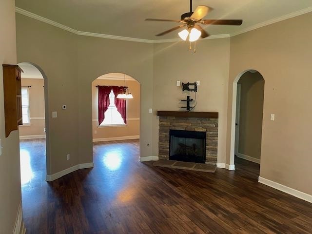 unfurnished living room featuring crown molding, a stone fireplace, ceiling fan, and dark wood-type flooring