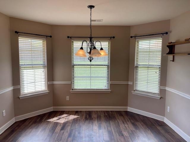 unfurnished dining area with an inviting chandelier, a wealth of natural light, and dark hardwood / wood-style flooring