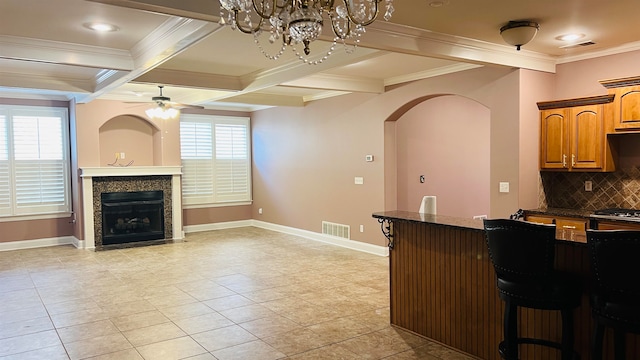 kitchen featuring decorative backsplash, a kitchen bar, ornamental molding, ceiling fan with notable chandelier, and light tile patterned floors