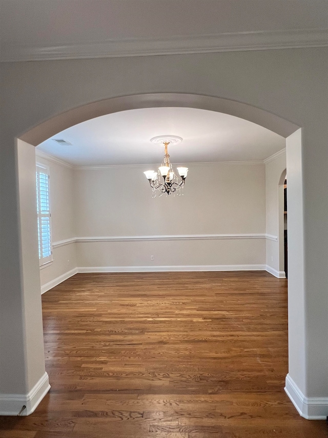 spare room with a chandelier, dark wood-type flooring, and ornamental molding