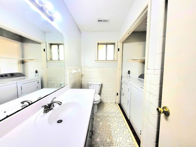 bathroom featuring vanity, a textured ceiling, separate washer and dryer, tile walls, and toilet