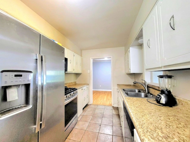 kitchen featuring appliances with stainless steel finishes, sink, light tile patterned floors, and white cabinetry