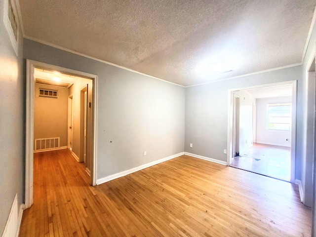 empty room featuring crown molding, light hardwood / wood-style floors, and a textured ceiling