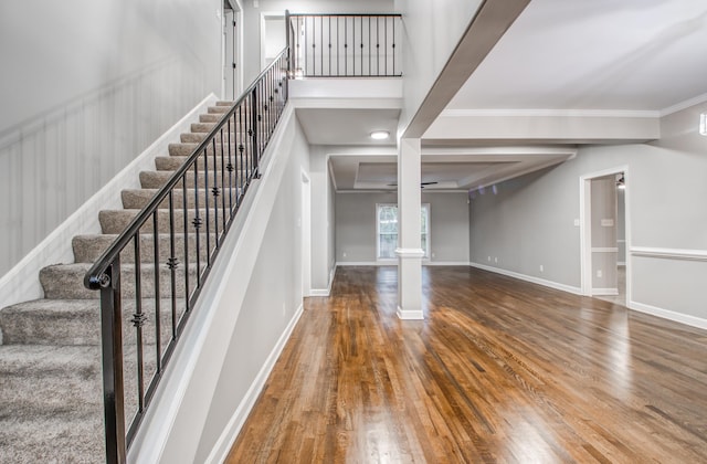 stairs with wood-type flooring and crown molding