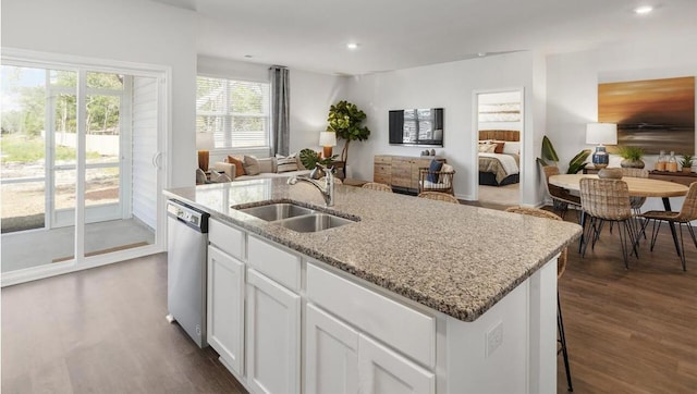 kitchen with an island with sink, white cabinets, stainless steel dishwasher, dark hardwood / wood-style floors, and sink